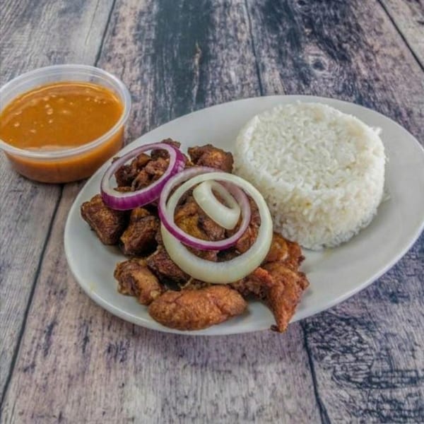 Fried meat with white rice, red and white onion rings, and a side of sauce.