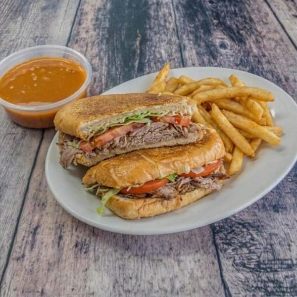 Two halves of a Cuban sandwich with fries and a side of dipping sauce on a white plate.