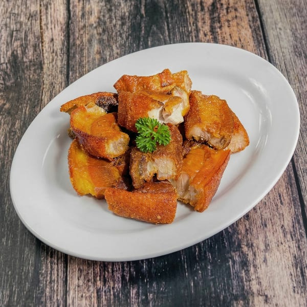 Crispy fried pork belly pieces, garnished with a sprig of parsley, on a white plate.