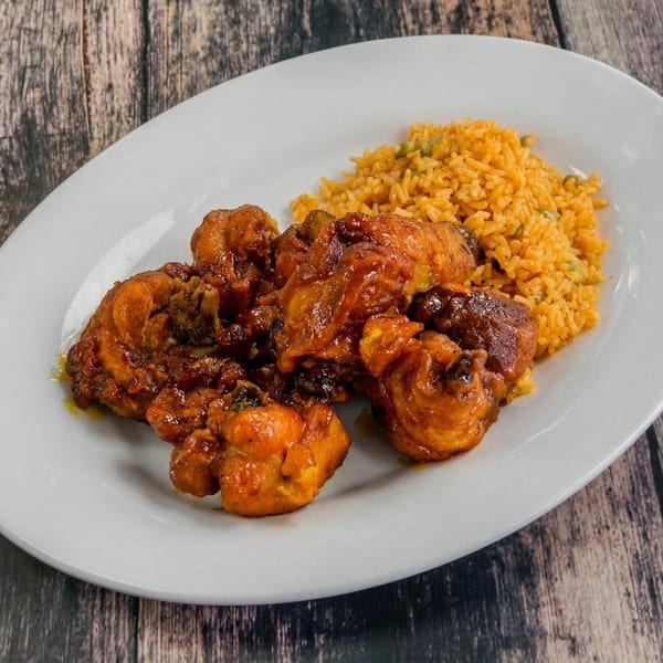 A white oval plate holds saucy brown chicken pieces and a side of yellow rice with green peas.