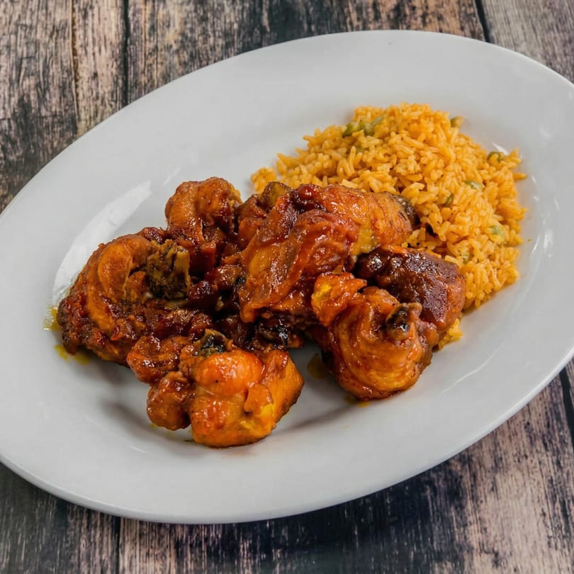 A white oval plate holds saucy brown chicken pieces and a side of yellow rice with green peas.