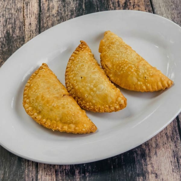 Three golden-brown fried empanadas with crimped edges on a white oval plate.