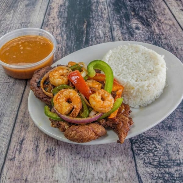 Grilled shrimp and steak with bell peppers, onions, and rice, served with a side of sauce.