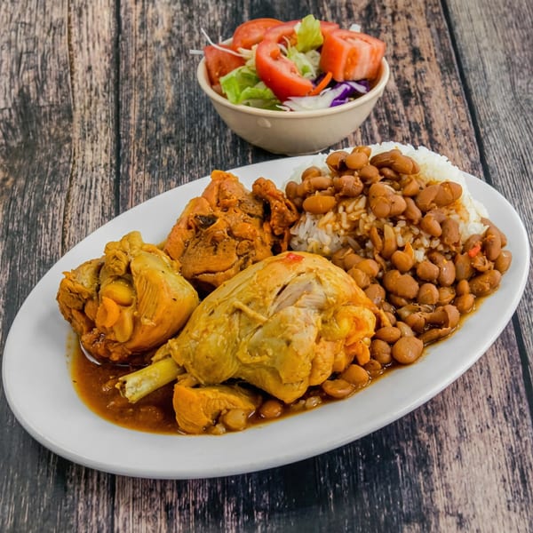 A plate of chicken, rice, and beans with a side salad on a wooden table.