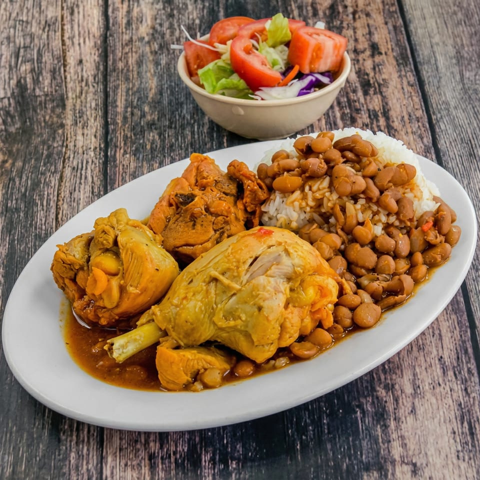 A plate of chicken, rice, and beans with a side salad on a wooden table.